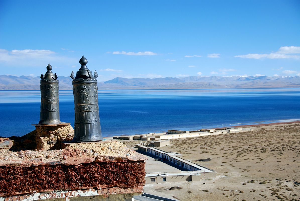 35 Victory Banners On Old Chiu Gompa Roof With Lake Manasarovar And Buildings Below Two victory banners are perched on the roof of the old Chiu Gompa with a view to Lake Manasarovar and some buildings below next to the lake.